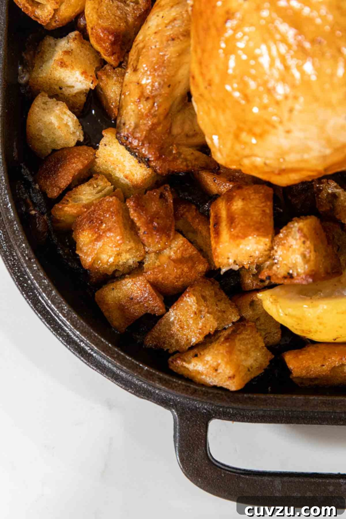 Ina Gartens Bright Lemon Chicken 7 Close up of golden croutons and vibrant lemon wedges complementing Ina Garten's lemon chicken in a cast iron pan, shimmering with pan juices.