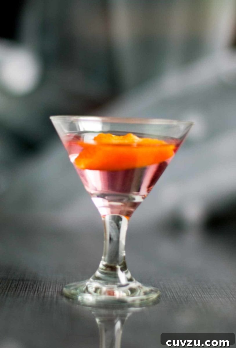 Stellar Surge 2 A vibrant red Cosmopolitan shot served in a small, elegant shot glass, garnished with an orange peel twist.
