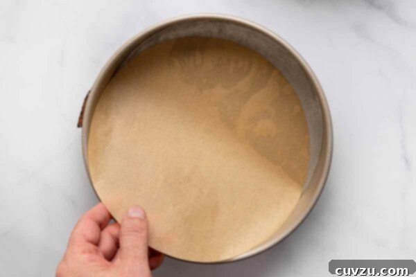 A person lining a cake pan with parchment paper.