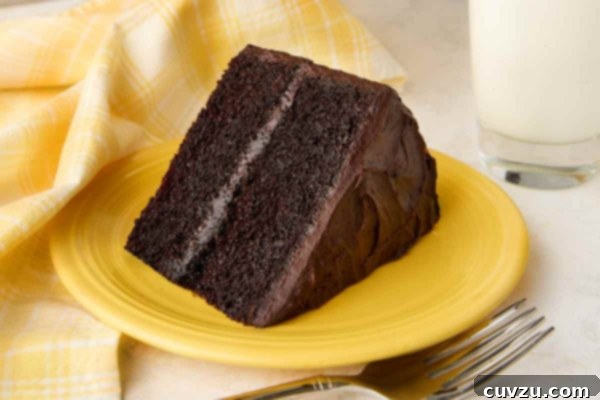 A slice of Hershey's chocolate cake with chocolate frosting on a yellow plate, with the remaining cake on a stand in the background.