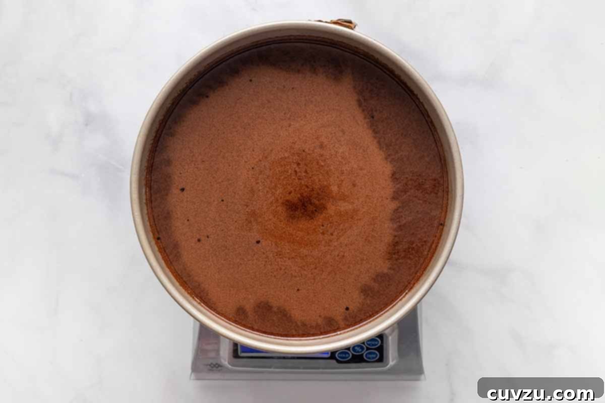 Next-Level Hershey's Chocolate Cake 8 A 9-inch round cake pan filled with rich chocolate cake batter, carefully placed on a digital kitchen scale. This image illustrates the professional tip of weighing batter for perfectly even cake layers, a detail that ensures consistent baking and a beautifully presented final dessert.