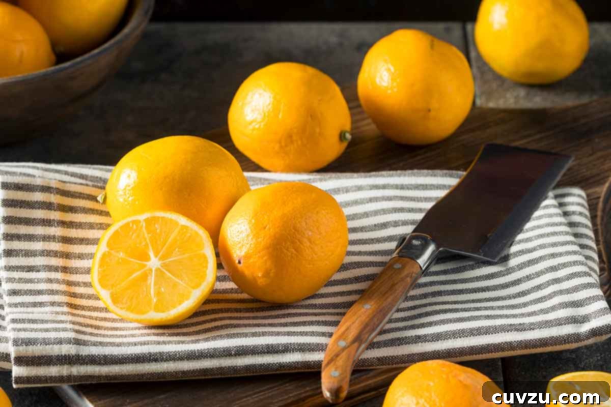 Fragrant Meyer Lemon Marmalade 4 Several plump Meyer lemons on a striped towel; one is elegantly sliced in half, revealing its juicy interior. Nearby rests a rustic cleaver.