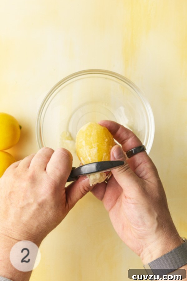 Fragrant Meyer Lemon Marmalade 8 A man's hand peeling a Meyer lemon with a vegetable peeler over a glass bowl.