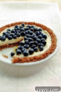 A blueberry pie with granola crust and blueberries on top with one slice missing.