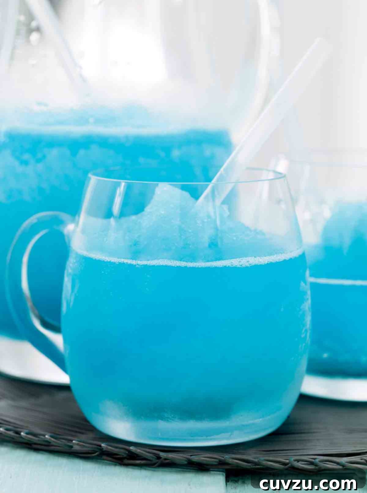 Neptune's Nectar 5 A pitcher and two glasses of blue margarita on a grey woven placemat, ready for a tropical getaway.
