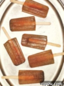 Six iced tea popsicles on a silver platter, garnished with fresh lemon slices and mint sprigs.