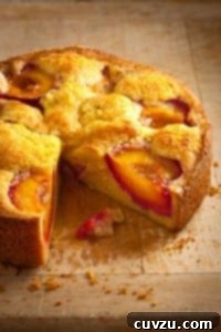 A round polenta plum cake on a wooden table with one slice cut from it.