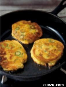 Okra Cornmeal Fritters 3 A close-up of three golden-brown okra cornmeal cakes, revealing slices of green okra, nestled in a cast iron skillet.