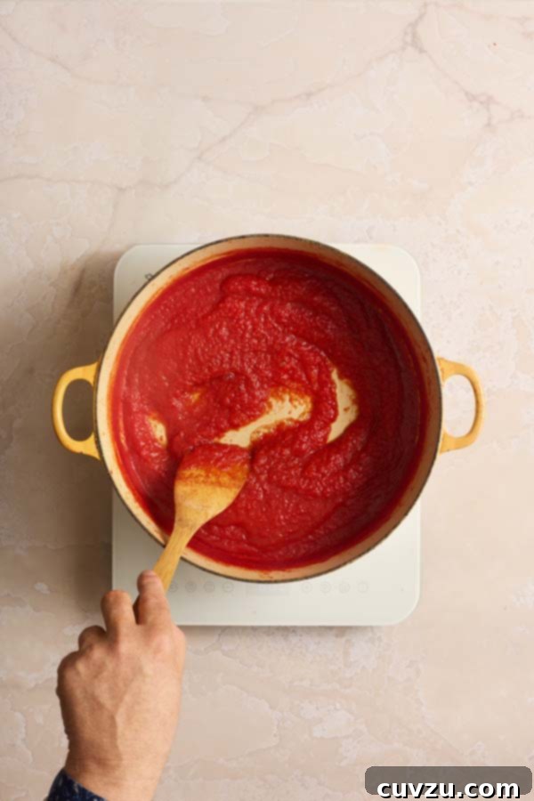 The Art of Homemade Tomato Paste 8 Stirring thick tomato purée as it simmers and reduces in a yellow pot on the stove.