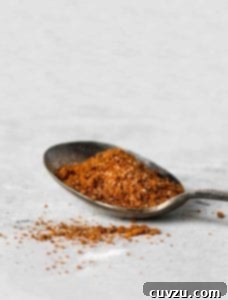 A spoon filled with Moroccan spice rub on a white surface with a little sprinkled beside the spoon.