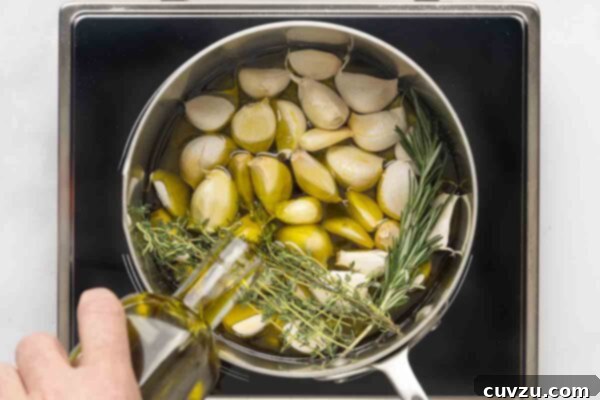 Golden Garlic Velvet 12 A person adding oil to a pot of garlic, thyme, and rosemary.