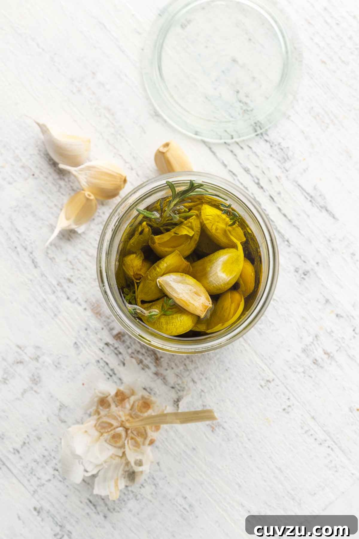 Golden Garlic Velvet 7 A sealed jar filled with golden garlic confit cloves immersed in oil, with several loose confit cloves scattered invitingly nearby on a rustic surface.
