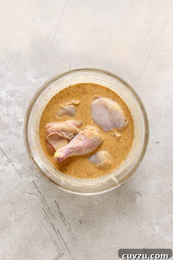 Effortless Extra Crispy Batter Fried Chicken 11 Raw chicken pieces marinating in a seasoned batter in a glass bowl.