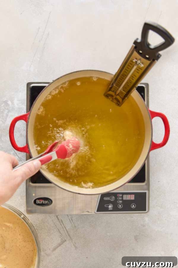 Effortless Extra Crispy Batter Fried Chicken 12 Using tongs to lower a piece of battered chicken into a pot of hot oil.