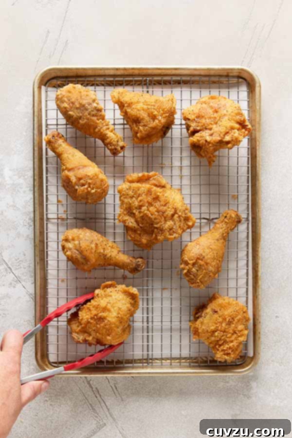 Effortless Extra Crispy Batter Fried Chicken 13 Golden, crispy fried chicken pieces draining on a wire rack set over a baking sheet.