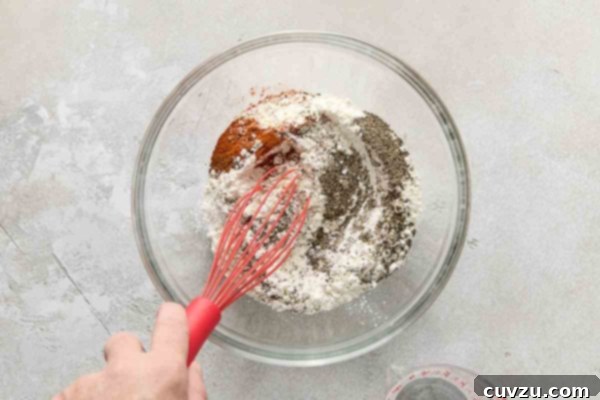 Effortless Extra Crispy Batter Fried Chicken 20 A person whisking a bowl of flour and spices to create batter for fried chicken.