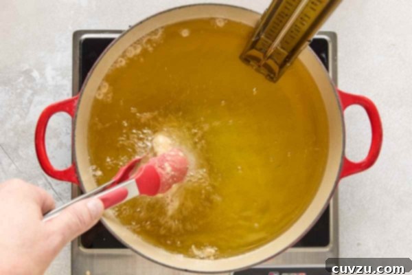 Effortless Extra Crispy Batter Fried Chicken 24 A piece of chicken being added to a pot of bubbling oil.