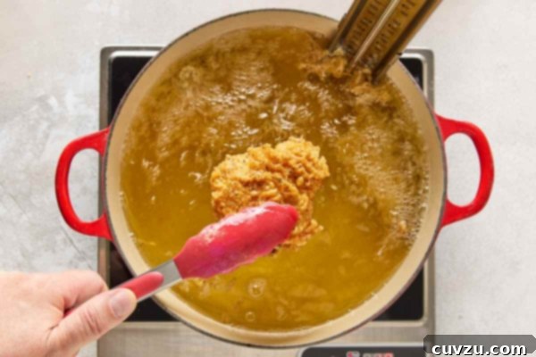 Effortless Extra Crispy Batter Fried Chicken 25 A piece of crispy fried chicken being lifted from a pot of bubbling oil.