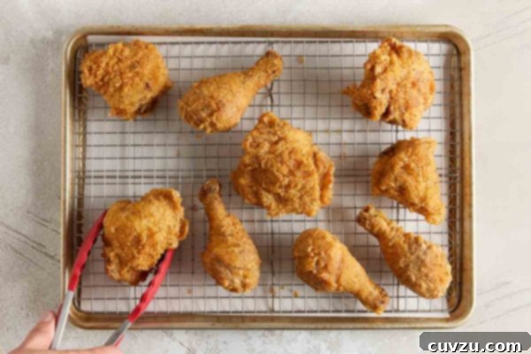 Effortless Extra Crispy Batter Fried Chicken 26 Pieces of crispy fried chicken cooling on a wire rack set over a baking sheet.