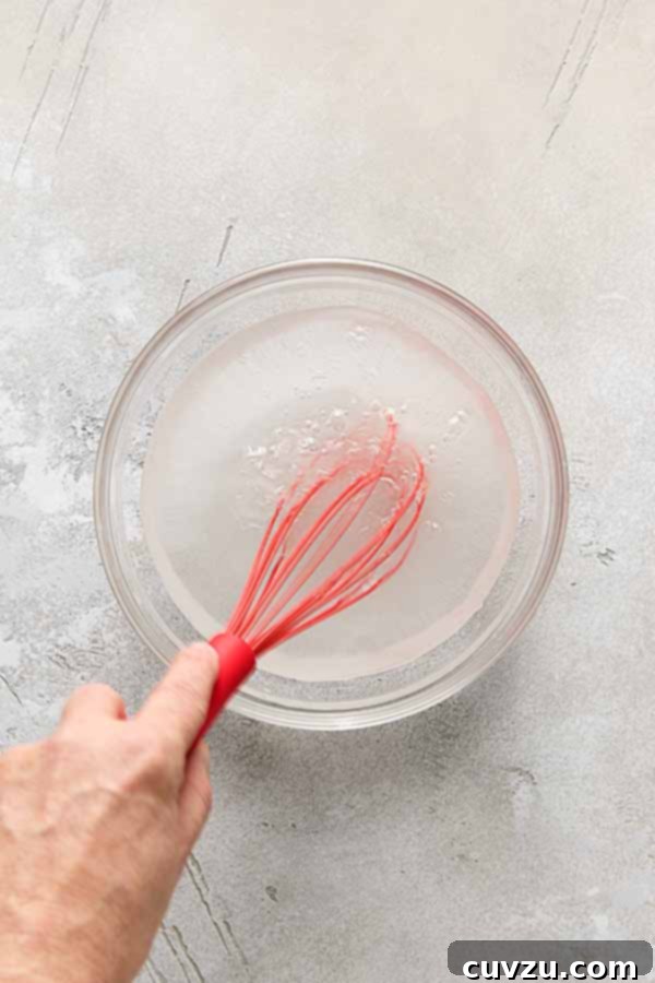 Effortless Extra Crispy Batter Fried Chicken 6 A hand whisking salt and sugar into water in a glass bowl to make a brine for fried chicken.