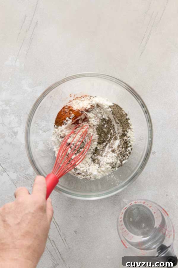Effortless Extra Crispy Batter Fried Chicken 8 A hand whisking flour and spices together in a glass bowl for the batter.