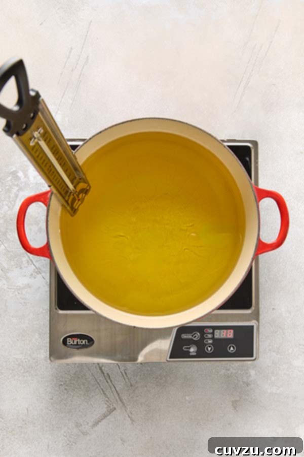 Effortless Extra Crispy Batter Fried Chicken 10 A Dutch oven filled with vegetable oil and a fry thermometer heating on a cooktop.