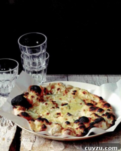 A wooden table with a white plate with parchment paper and Jim Lahey's white pizza, with a stack of glasses in the background.