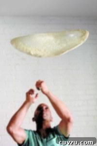 A thin circle of stretched pizza dough being tossed in the air, captured mid-flight.