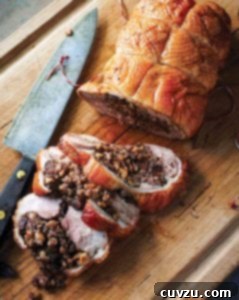 Golden Roast Duck with Farro, Fig & Hazelnut Stuffing 4 A roast duck stuffed with farro, figs, and hazelnuts, with three slices cut from it on a wooden cutting board with a knife resting beside it.