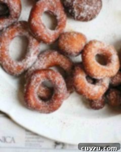 A pile of sugar-dusted easy raised doughnuts on a white plate, showcasing their inviting golden-brown texture.