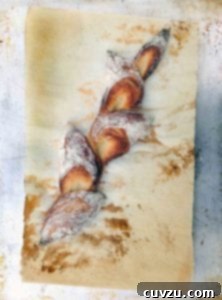 A baked pain d'epi, showcasing its beautiful wheat sheaf shape, on a piece of parchment paper.