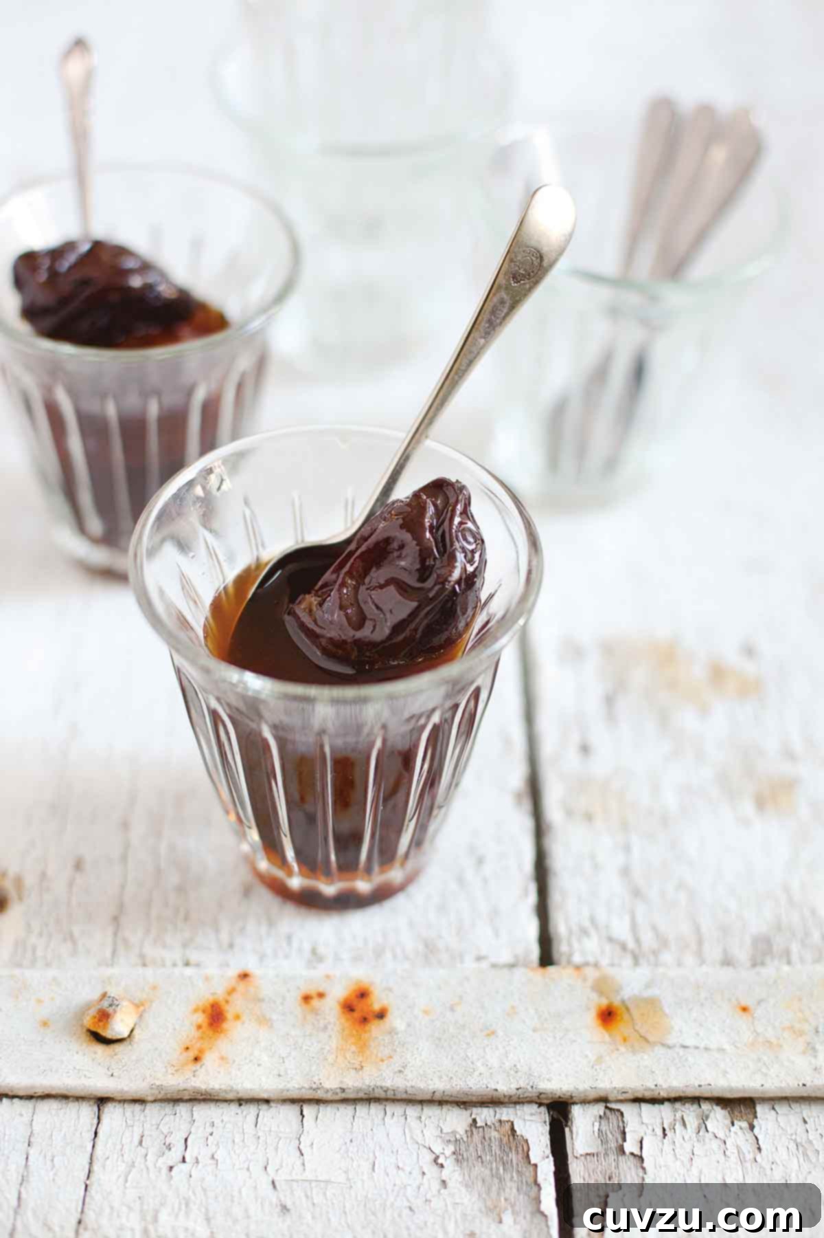 Decadent Rum Prunes 2 Two small glasses filled with prunes in rum, each with a spoon resting inside, showcasing the rich, dark fruit.