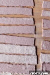 Strips of homemade red wine pasta on a wooden surface.
