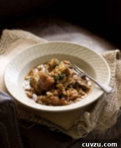 A white porcelain bowl filled with cassoulet and a fork rests on the side.