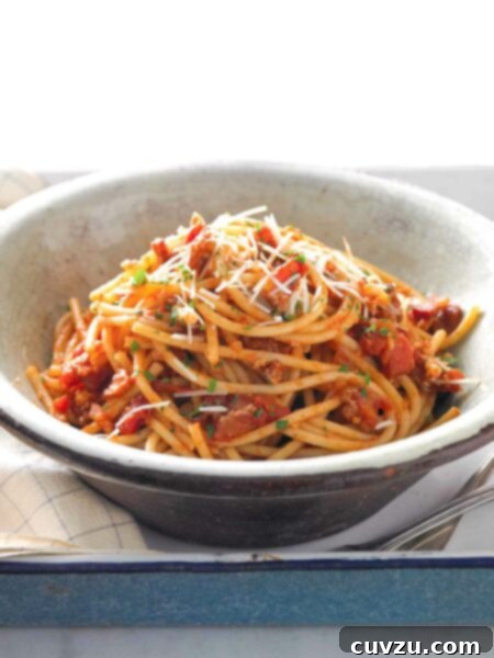 A brown and white pottery bowl filled with bucatini all'Amatriciana, topped with pecorino and parsley.