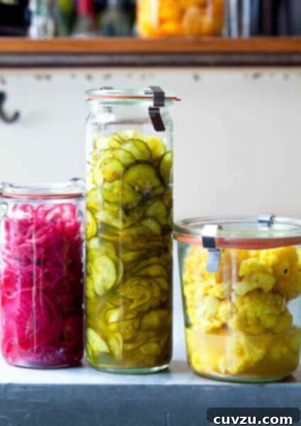 Three jars of Israeli pickles, one with cauliflower, one with cucumbers, and one with red onion.
