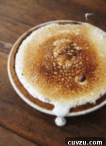 A s'mores pie on a wooden table with some topping leaking from the pie.