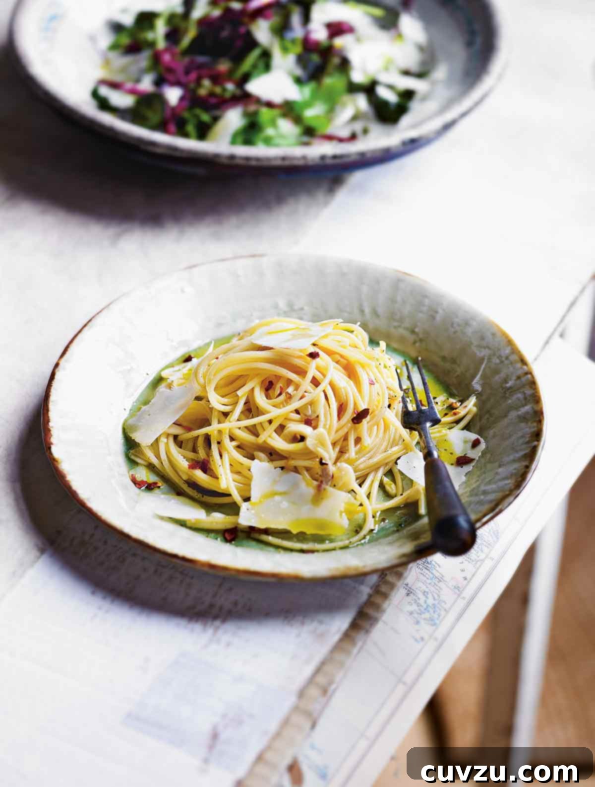 A glistening bowl of Spaghetti all'Aglio e Olio, topped with fresh parsley, red pepper flakes, and finely grated Parmesan cheese.