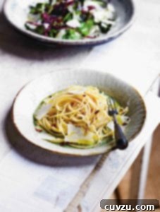 A bowl of spaghetti all'Aglio e Olio topped with olive oil and flakes of Parmesan cheese.
