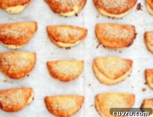 Twelve Turkish borekitas sprinkled with sesame seeds on a piece of parchment.
