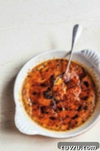 A shallow white dish filled with coffee creme brulee, with a spoon resting inside.