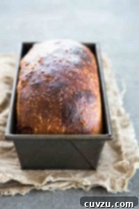 A browned loaf of homemade sandwich bread in a metal loaf tin, sliced and ready to eat.