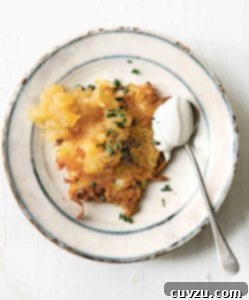A cheddar and potato latke topped with chives and applesauce on a plate with a spoonful of sour cream beside the latke.