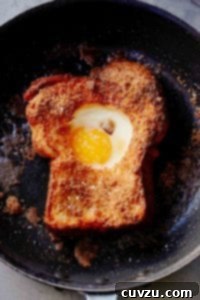 A slice of toast in a skillet with an egg cooked into the center hole of the toast, ready to be served.