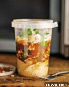 Plastic container of North African chicken soup with shredded chicken, ras el hanout, couscous, and preserved lemon