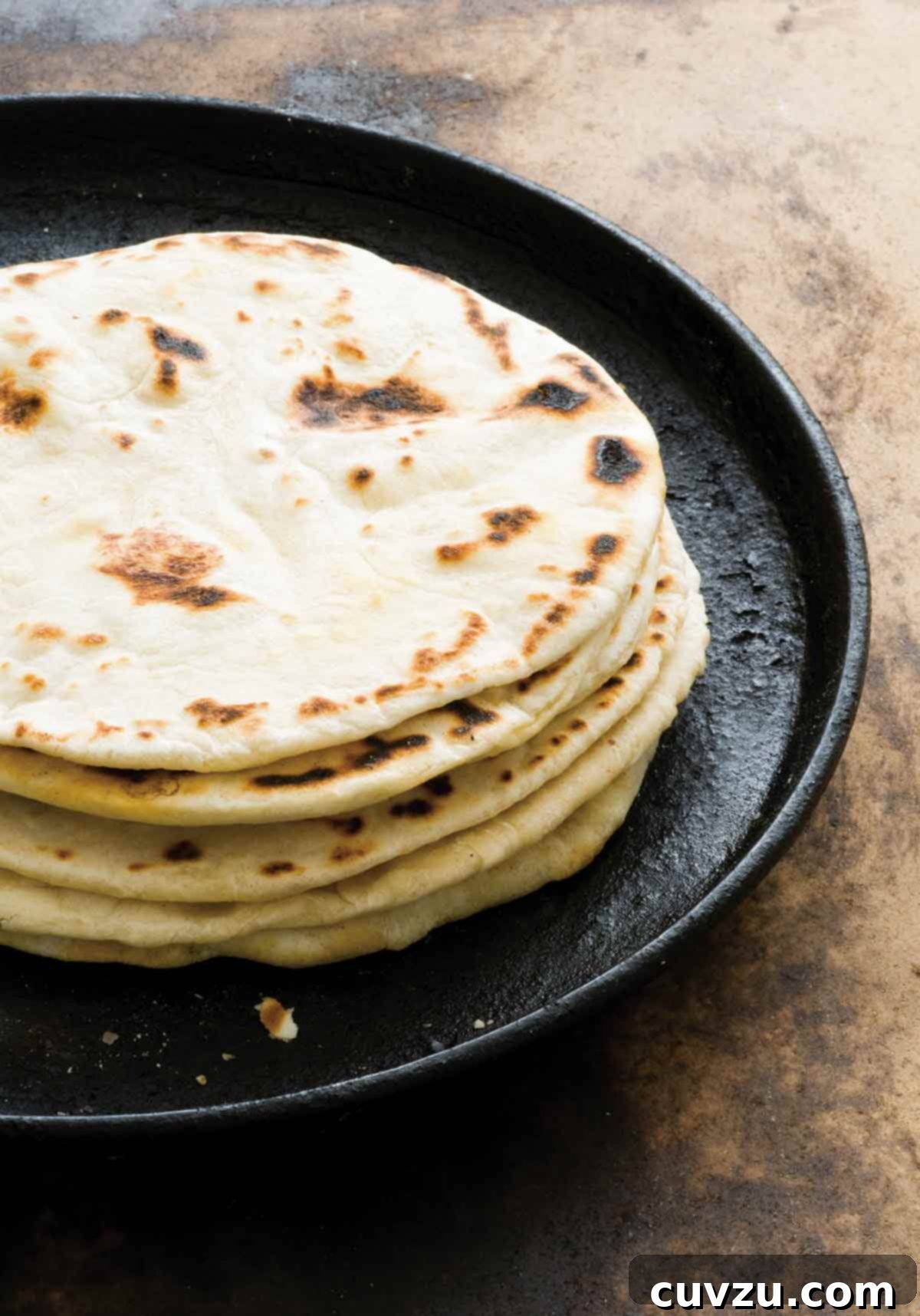 Smoky Bacon Fat Flour Tortillas 2 A stack of golden brown, homemade flour tortillas with bacon fat, resting on a rustic cast-iron skillet, ready to be enjoyed. The tortillas exhibit a soft, pliable texture, hinting at the savory depth of flavor within.