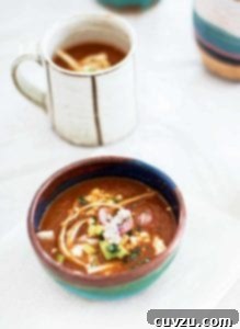 A pottery bowl filled with tortilla soup, garnished with radish, cotija cheese, tortilla strips, and avocado.