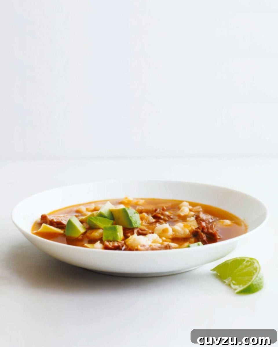 Effortless Weeknight Pork Posole 2 A vibrant white bowl filled with quick posole with tender pork, adorned with fresh avocado slices and a zesty lime wedge on the side, ready to be enjoyed.