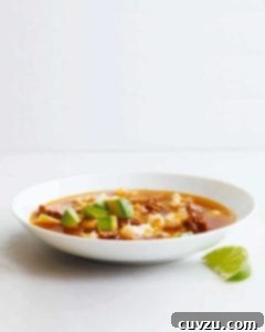 Effortless Weeknight Pork Posole 3 A white bowl filled with quick posole with pork topped with avocado with a lime wedge on the side.
