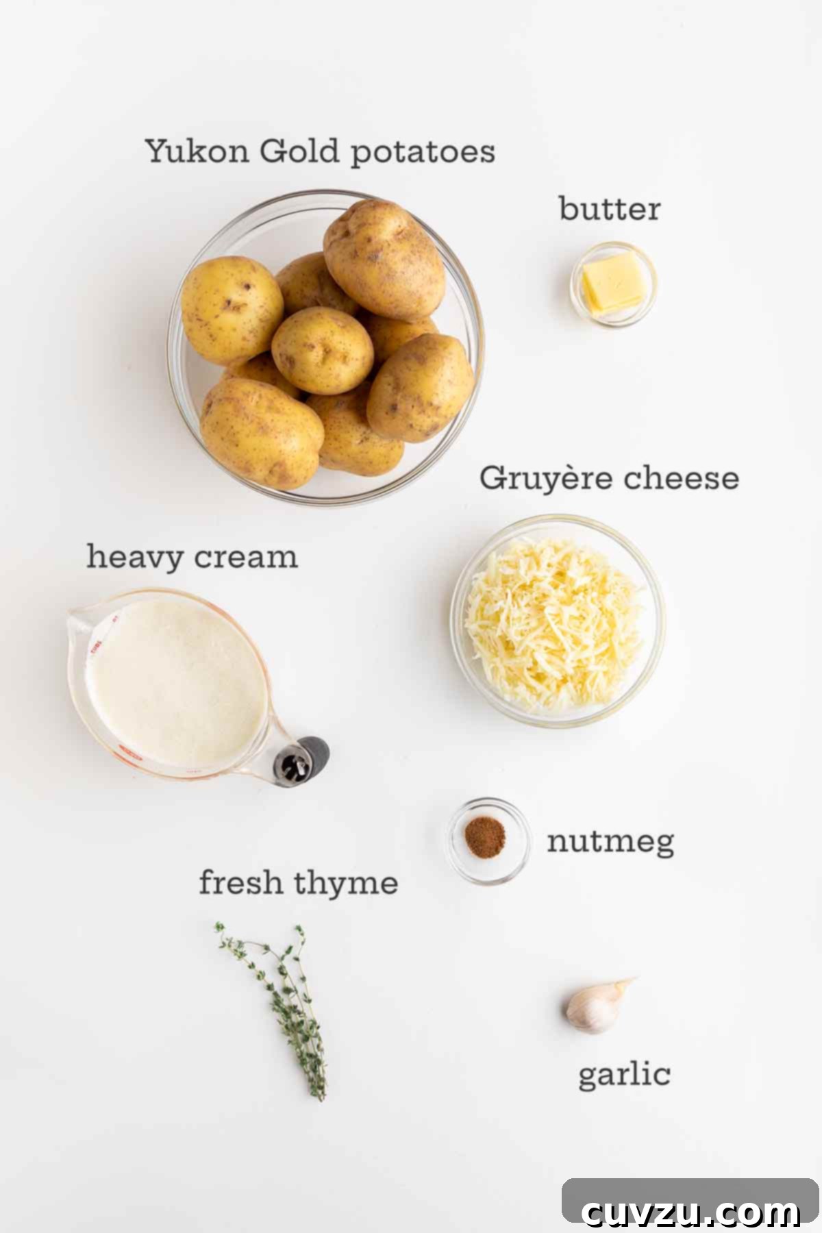 A beautiful arrangement of fresh ingredients for potatoes dauphinoise: golden Yukon Gold potatoes, a block of rich butter, a generous wedge of Gruyère cheese, a carton of heavy cream, a hint of nutmeg, sprigs of fragrant thyme, and cloves of aromatic garlic.